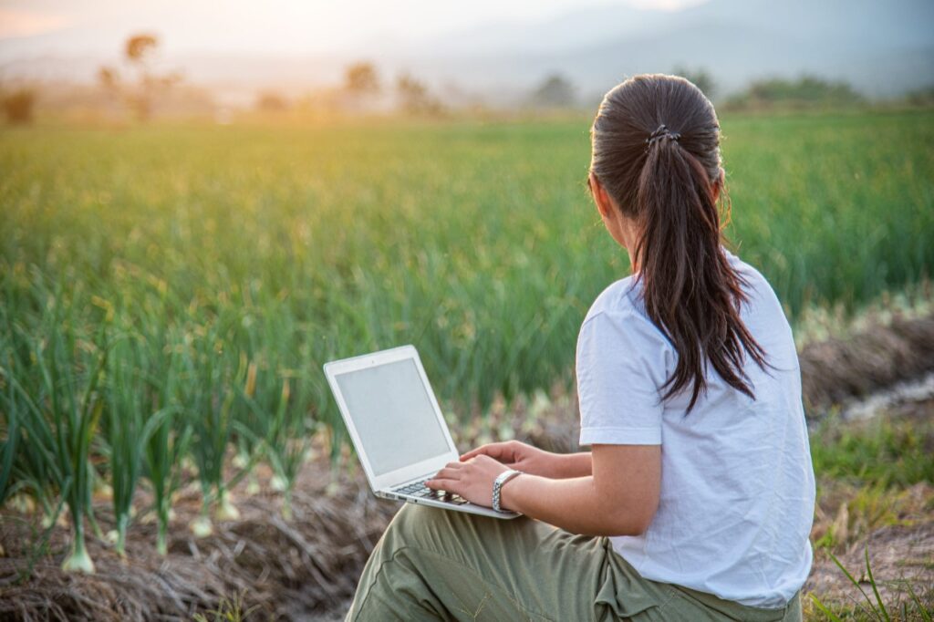 Woman with laptop looking at a farm field.